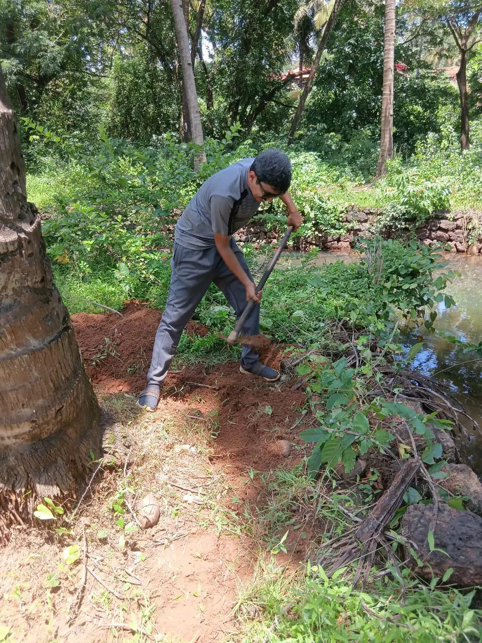 A person using a hoe to dig red soil beside a narrow water channel